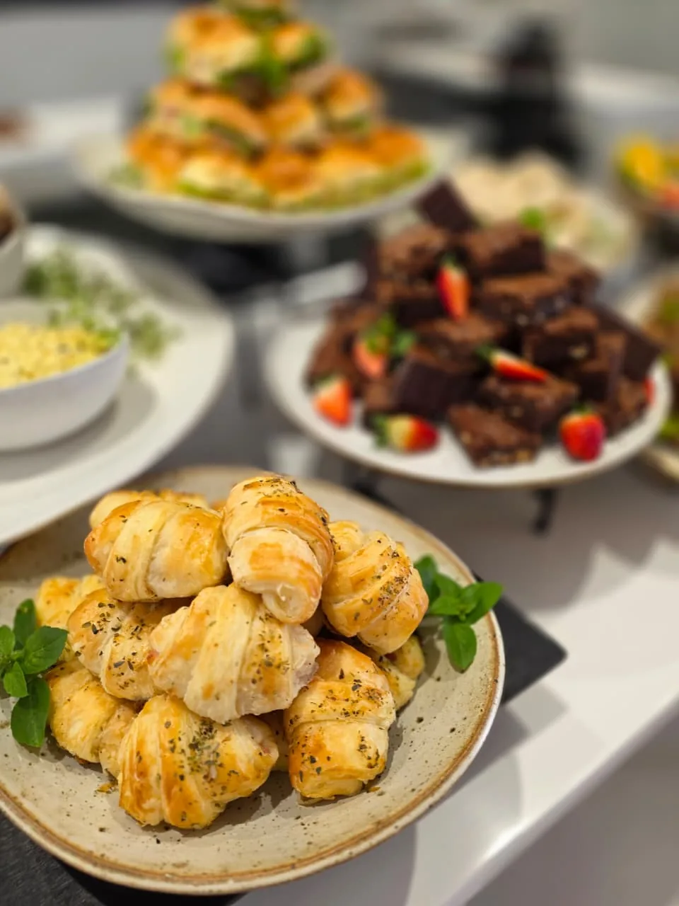 Mesa de café com pãezinhos artesanais, brownies e frutas frescas