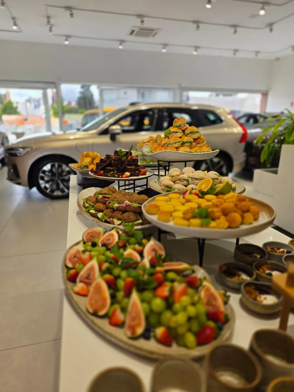 Buffet completo servido em evento corporativo de concessionária, com tábuas, salgados e sucos naturais